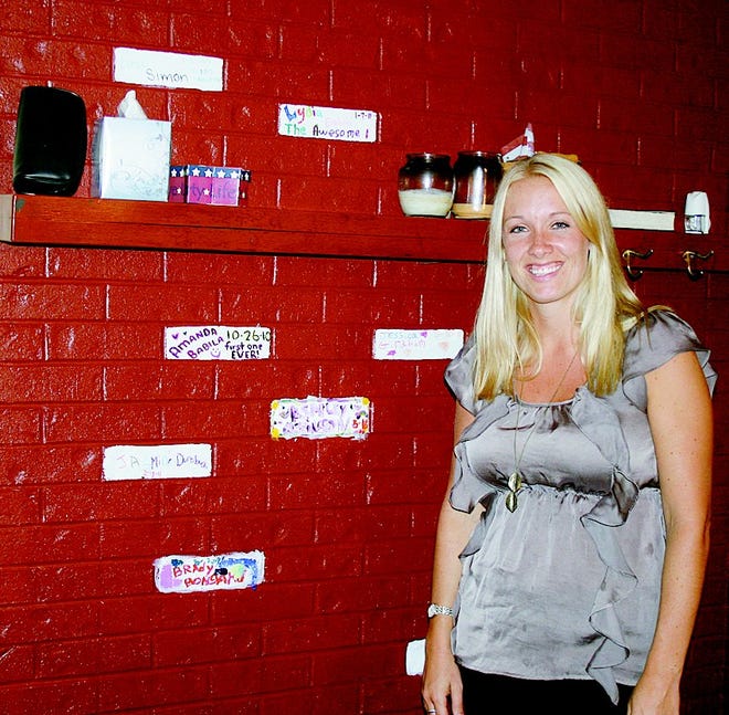 Judy’s Youth Transition Home Chief Administrator Danielle Lawson stands at the home’s welcome wall. Each client decorates a brick upon acceptance into the program. “We always have a blank brick ready,” she said.