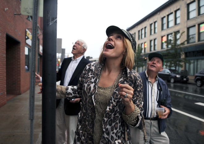 Relatives of Carol Mathers, who is pictured in an outdoor photo exhibit in downtown Brockton, react after viewing her portrait on a Main Street building. Susan Mathers, center, her father Tom Gianouloudis, right, and her father-in-law Cortland Mathers, husband of Carol Mathers, look over the photo.
