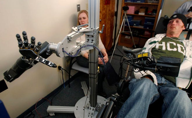 In this photo made Sept. 21, assistant professor Jennifer Collinger, left, watches as quadriplegic research subject Tim Hemmes operates the mechanical prosthetic arm in a testing sessions at a University of Pittsburgh Medical Center research facility in Pittsburgh. Hemmes had a chip implanted on the surface of his brain that reads his intention to move his paralyzed arm and sends that instruction instead to an advanced bionic arm. The goal is to create mind-controlled prosthetics to restore some independence to the paralyzed. (The Associated Press)