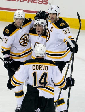 Bruins' Benoit Pouliot (67); Joe Corvo (14); and Zdeno Chara (33) celebrate with Brad Marchand, center, following Marchand's goal against the Carolina Hurricanes during a game in Raleigh, N.C., on Wednesday. Carolina won 3-2. Tonight, the Bruins take on the Blackhawksk in Chicago.