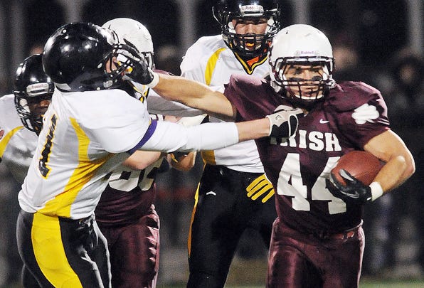 Aquinas running back Billy Lombardi gives a stiff arm to try and avoid a tackle from McQuaid's Duncan Ayer.