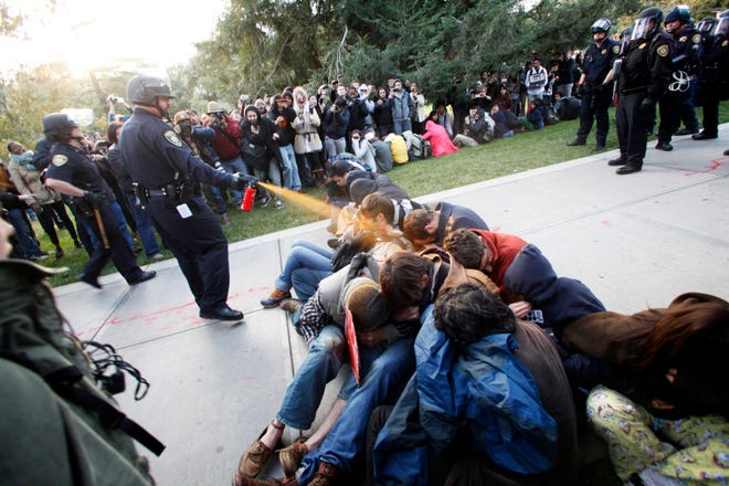 In this Friday, Nov. 18, 2011, photo University of California, Davis Police Lt. John Pike uses pepper spray to move Occupy UC Davis protesters while blocking their exit from the school's quad Friday in Davis, Calif. Two University of California, Davis police officers involved in pepper spraying seated protesters were placed on administrative leave Sunday, Nov. 20, 2011, as the chancellor of the school accelerates the investigation into the incident. (AP Photo/The Enterprise, Wayne Tilcock)