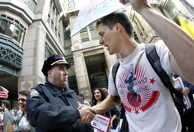 In this file photo taken Wednesday, Oct. 5, 2011, an Occupy Boston protester shakes hands with a police officer after a rally in Boston's financial district. In the first two months of the nationwide Occupy Wall Street protests the movement has cost local taxpayers at least $13 million in police overtime and other municipal services, according to a survey conducted by The Associated Press. (AP Photo/Elise Amendola, File)