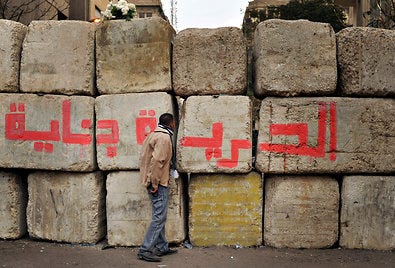 A concrete barricade in Cairo is sprayed with graffiti that reads “Freedom is coming.” The barrier blocks a street connecting Tahrir Square and the Interior Ministry.