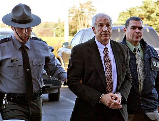 This Nov. 5, 2011 file photo shows former Penn State football defensive coordinator Jerry Sandusky, center, wearing handcuffs as he is escorted to the office of Centre County Magisterial District Judge Leslie A. Dutchcot, in State College, Pa.