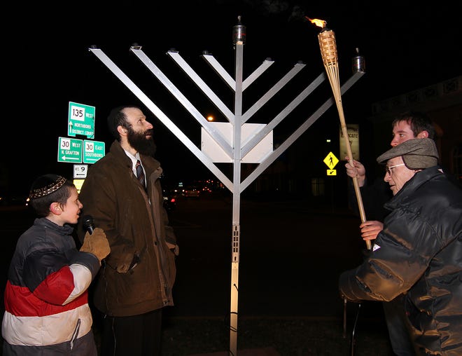 Rabbi Michoel Green, second from left, of Chabad of Westborough, asks Westborough resident and veteran, George Miller, right, to light the Menorah to celebrate the beginning of Chanuka on Tuesday evening on the Rotary. At left is Moishe Green, 11, also honored by his father, who spoke the prayers during the ceremony.