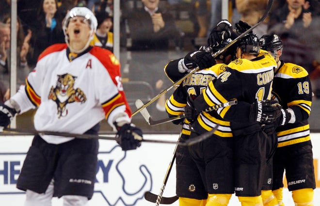 Boston Bruins' Dennis Seidenberg, center, celebrates in a huddle with teammates Joe Corvo and Tyler Seguin (19) as Florida Panthers' Tomas Kopecky, left, skates away after the Bruins scored their fourth goal in the first period of an NHL game in Boston, Friday, Dec. 23, 2011.
