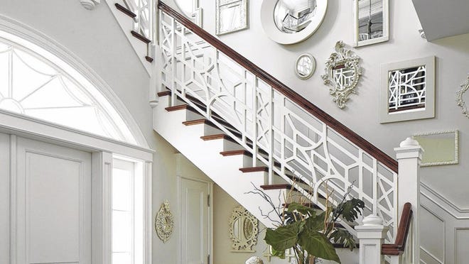 With its fanciful fretwork bannister, the foyer’s staircase marches to a mid-landing and then continues above the front door. Palm Beach decorator Jack Fhillips used white-framed mirrors to bounce natural light into the space. The floor is covered in marble.