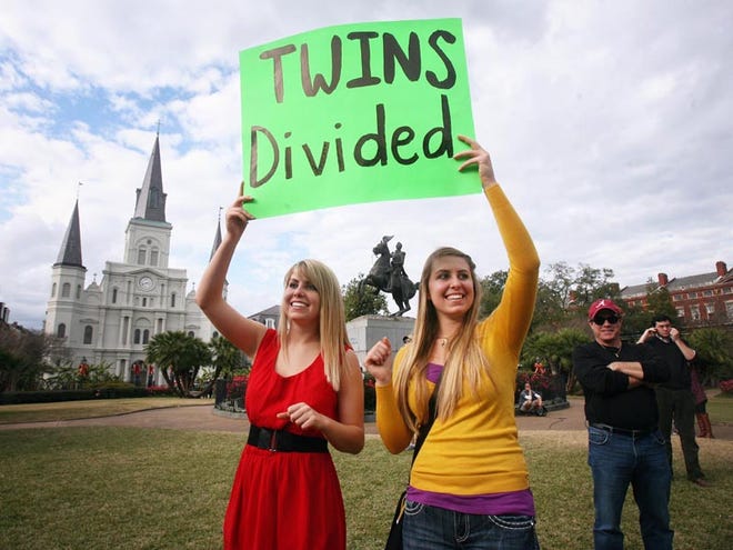 From left, twin sisters Victoria and Brittany Nutting of Diamond Head, Miss., pull for opposing teams. They hold up a sign in the background of an ESPN filming at Jackson Square in New Orleans on Friday.