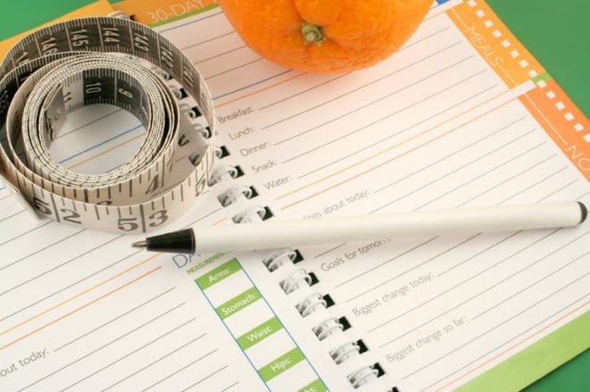 writing in a diet and nutrition journal with orange to the
side