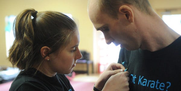 Ashley Gilbert, left, pins a blue child abuse awareness ribbon onto the shirt of her husband, Sensei Anthony Gilbert, owner and head instructor of Pocono Crimson Dragon in Pocono Summit on Saturday.