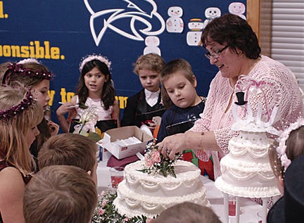 First graders at Lincoln Elementary School celebrated the marriage of Mr. Q and Miss U on Monday. Students dressed up in their best for the annual ceremony, in which Q was asked to take U with him wherever he went and make the best words possible. Here, Mrs. Possamai cuts the cake for “wedding guests”?to enjoy at the reception.