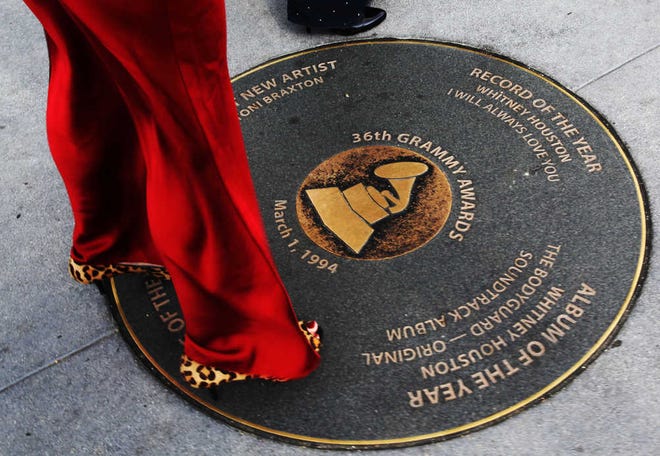 A woman arriving for Sunday's Grammy awards looks at a Grammy sidewalk plaque, honoring Whitney Houston's wins for Record of the Year and Album of the Year in the the 36th Grammy Awards, outside the Grammy Museum in Los Angeles. Houston died Saturday, Feb. 11, 2012, on the eve of the 54th Grammys, at the Beverly Hilton Hotel, where she was preparing to attend a pre-Grammy party. She was 48.