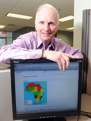 Charlie Fiske leans against a computer monitor displaying the continent of Africa.