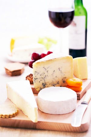 Assortment of cheeses and knife on wooden cheese board, close-up, glass and bottle of red wine in background