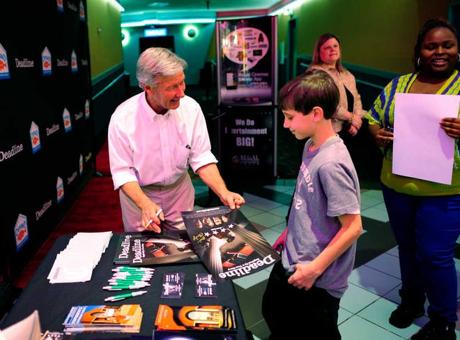 Mark Ethridge signs a poster for John Hanyok, 13, during the Augusta premiere of the film Deadline at Regal Augusta Exchange Stadium 20. Ethridge wrote the screenplay for the film, which is based on a true story adapted from his novel Grievances.