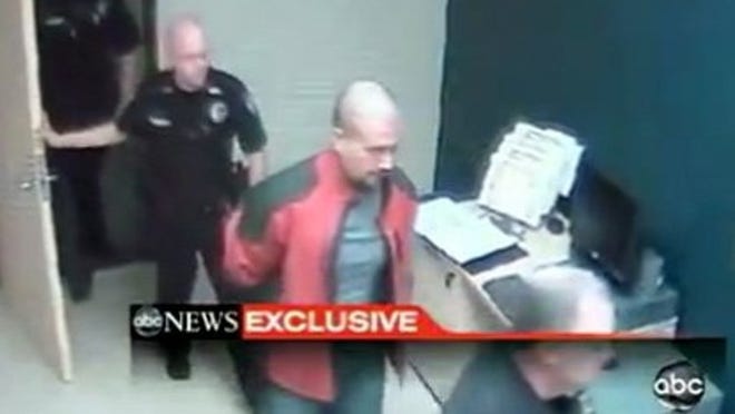 In this image taken from video at the Sanford, Fla., Police Department, George Zimmerman, in red jacket, is escorted into the Sanford police station in handcuffs on Feb. 26, 2012, the night he fatally shot Trayvon Martin.