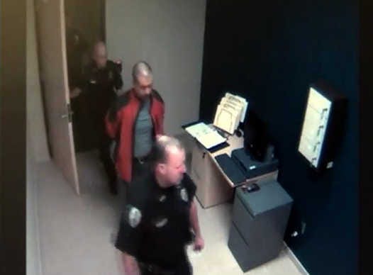 In this image taken from video at the Sanford, Fla., Police Department, George Zimmerman, center, is escorted into the police station in handcuffs on Feb. 26, the night he fatally shot Trayvon Martin.
