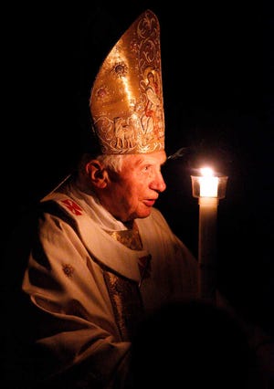 Pope Benedict XVI, holding a tall, lit, white candle, enters a hushed and darkened St. Peter's Basilica, at the Vatican Saturday, April 7, 2012, to begin the Vatican's Easter vigil service. Except for the twinkle of camera flashes, the basilica was almost pitch-black as the thousands of faithful in pews awaited Benedict's arrival through the rear entrance Saturday night. Christians on Easter joyously mark their belief that Christ rose from the dead after his crucifixion. Praying at the start of the service, Benedict said Easter brings hope to the faithful. On Sunday morning, he will lead Easter Mass in St. Peter's Square. (AP Photo/Pier Paolo Cito)