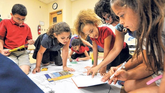 Evan Trabusana, 9; Elisa Leon, 8; Mya Robinson, 8; Center for Creative Education artist Ronni Gerstel; and Madison Fleri, 8, refer to a picture of the Main Building on Ellis Island while coloring a picture in their classroom at Hidden Oaks Elementary.