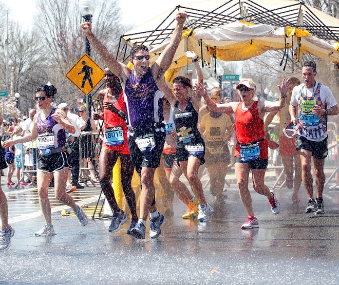 From Foxborough Stephen Diprete (center) raises his arms as he goes through a water spray, courtesy of the Natick fire department during Monday morning's Boston marathon in Natick Center.