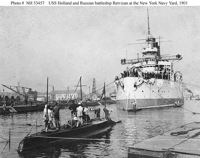 The USS Holland (Submarine Torpedo Boat No. 1) at the New York Navy Yard, Brooklyn, New York, in October 1901. In the background is the Russian battleship Retvizan, then nearing final completion after being constructed by the Cramp shipyard, Philadelphia.