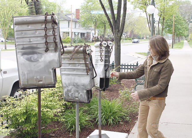 Jennifer Meyer of Lansing. Ill., checks out the placement of her “Three Old Furnace Fellows” in front of Martin's Home Center. Meyer’s art is made out of the heat exchangers from her old furnace and other recycled metal.