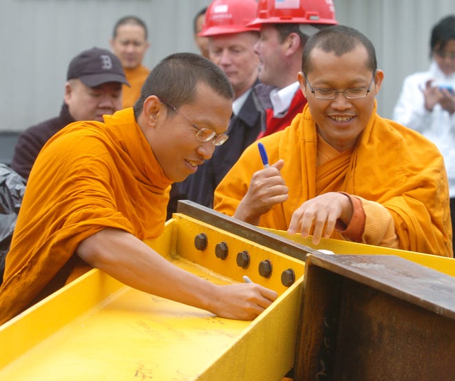 Buddhist monks Pramuan Buddee, left, and Manit Sagolla sign a beam to be raised to the top of the temple at the topping off ceremony for the Thai Buddhist Temple in Raynham on Thursday.