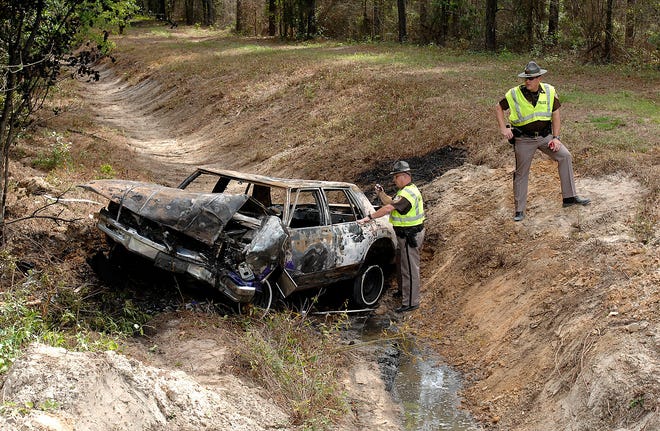 Glynn County traffic officer Gary Corey, left, investigates a single car crash on Altamaha Park Road in which a 1986 Pontiac left the roadway, hit a tree and burned in a drainage canal. The driver and only occupant was airlifted to a trauma center.