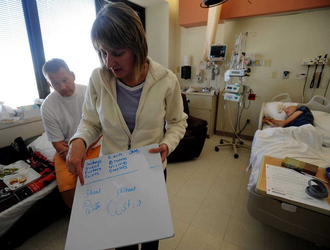 Lisa Chontos shows the writing progress of her son, Austin, while her husband, Michael Chontos, sits on the side of a fold-up bed in their son's hospital room in the Pediatric Intensive Care Unit of The Children's Hospital at Northwest Texas Hospital. Austin Chontos, a Randall High School sophomore, was injured April 14 while at bat during a game against Caprock High School.