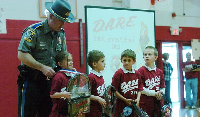 D.A.R.E. State Police Lt. Tim Madden awards first place to Victoria Watt, left, a first grade student at Saint James School Thursday during graduation ceremonies at the Danielson school. From left are runners up Cameron Seiffert, Cameron Sauer and Nathan Barnwell.