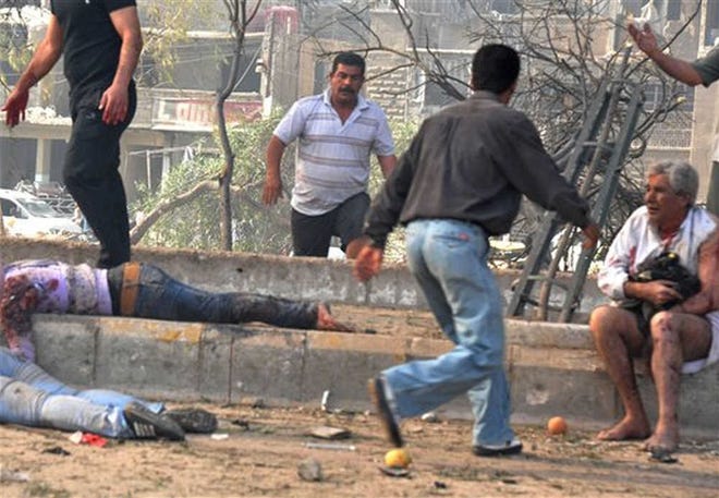 Men run between the dead and the injured at the scene of two bombings yesterday in the Qazaz neighborhood of Damascus.