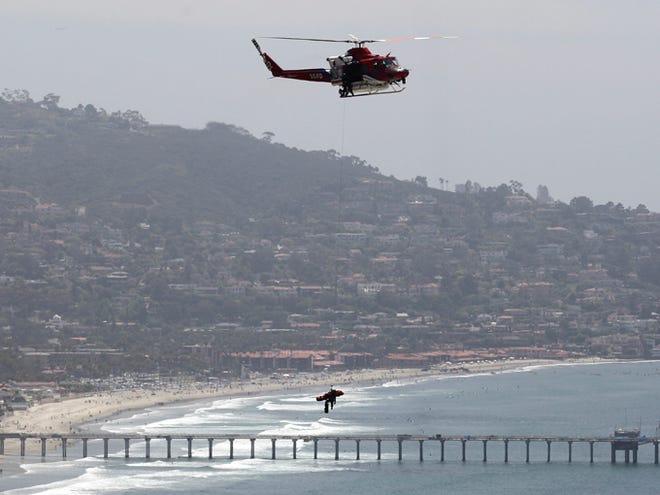 A San Diego firefighter suspended from a helicopter on a line holds on to a rescue basket containing the body of a woman Saturday as it flies over the La Jolla section of San Diego. Pamela Hargett, 52, of Inman, was paragliding along the Torrey Pines cliffs when she apparently lost control and crashed into the cliff sides.