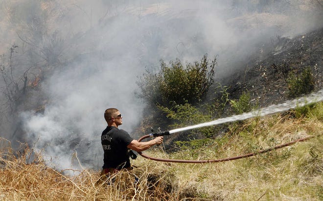 Tucson firefighter Lyle Steffens sprays water on a brush fire in midtown Tucson, Ariz., on Thursday. Firefighters responded to multiple brush fires, whipped-up by wind and low humidity.