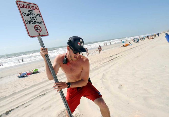 Carolina Beach Ocean Rescue squad leader Evan Anderson places a sign in the sand closing the beach to swimming at Carolina Beach, N.C. Saturday, May 26, 2012. Strong rip currents created dangerous swimming conditions and prompted Carolina Beach Ocean Rescue to close the beach to swimming and not allow people in past their knees. (AP Photo/The Star-News,Matt Born )