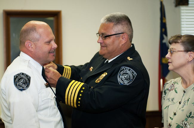 Thomasville Police Chief Jeff Insley pins bars on the collar of newly promoted Capt. Mark Kattner as Kattner's wife, Leigh Ann, looks on Thursday morning in Thomasville's City Council chamber.