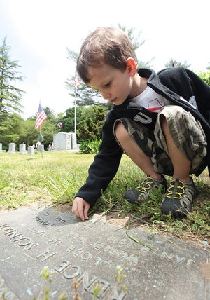 Ben Wilder, 4, of Scituate places a penny on a veteran's footstone while honoring the veterans buried at Cudworth Cemetery after the Memorial Day ceremonies. The pennies are a Wilder tradition to honor the veterans who have fought for their country. Ben's brother, Ian, is joining the National Guard.