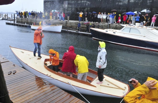 Rain-soaked International Yacht Restoration School graduates celebrate with a champagne shower on Saturday while launching their Herreshoff design Watch Hill 15 sailboat during the school’s commencement ceremony in Newport.