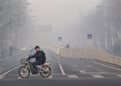 In this Jan. 10, 2012 file photo, a man rides an electric bike crossing a street shrouded by haze in Beijing.