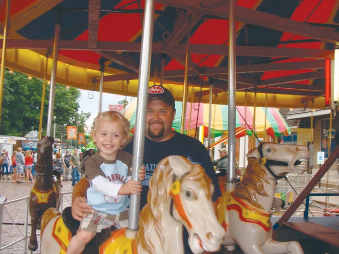 Kade Schieber, 2, and his dad, Brian, of Metamora ride the merry-go-round at Old Settler’s Days last year.