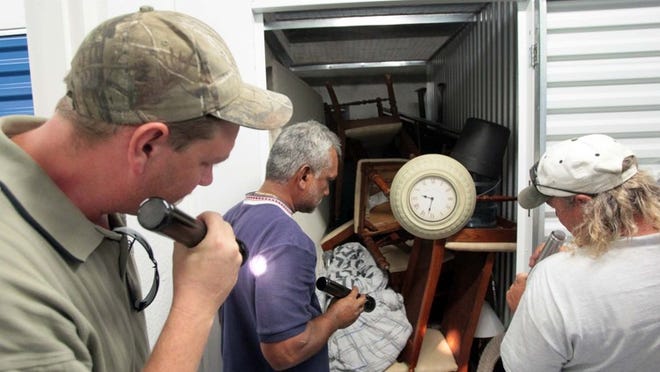 Dustin Acker of Boynton Beach (left) and LaDon Tumelson of Boca Raton (right) and a unidentified bidder take a peek inside a storage unit that was up for auction at Lantana Self Storage. The winning bid was $150. The owner of the unit owed $389.22.