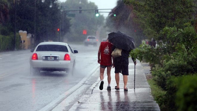Pedestrians share an umbrella to shelter from the rain Sunday afternoon as they walk along Federal Highway in Lake Worth.