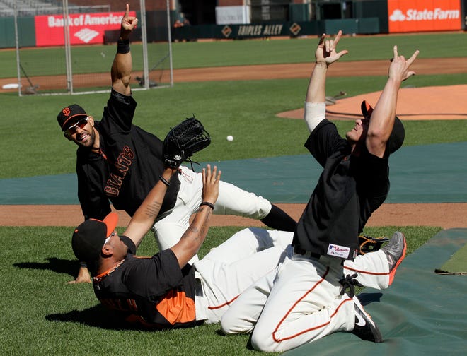In this Tuesday, June 26, 2012, photo, San Francisco Giants center fielder Angel Pagan, rear, signals as catcher Hector Sanchez, bottom, and Ryan Theriot play around before a baseball game against the Los Angeles Dodgers in San Francisco. The Giants' friendly new center fielder has been as reliable in the clubhouse as he has on the diamond in the first half. The 31-year-old considers his brief stint studying English in community college among the best decisions he ever made.
