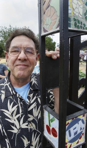 Artist John Comunale stands next to the gate he designed for the Feed My Sheep Garden at the First Congregational Church as part of the University of Akron's Arts LIFT program in Akron.  (Paul Tople/Akron Beacon Journal)