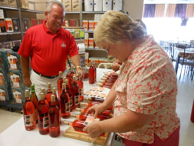 Ray Rovira, co-owner of Vino Fabbricanti, helps Cheryl Albrecht of Massillon put foil caps on her custom-made Watermelon White Merlot. Rovira went to SCORE for planning advice before opening his 2-year old shop in Canton.