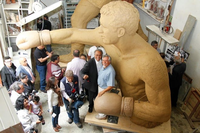 Sculptors Victor Gutierrez, left, and Mario Rendon, in light blue shirt, show off the top half of the clay model they are building for the Rocky Marciano statue in Mexico City. The sculptors and World Boxing Council, which is paying for the Brockton-bound statue, held a press conference to announce the statue is 70 percent done.