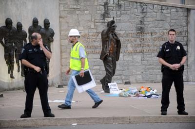 Police and construction workers have surrounded the Joe Paterno statue in State College, Pa., Sunday, July 22, 2012. A chain-link fence has been erected around the perimeter surrounding the statue. Two dump trucks, a flatbed truck and a forklift that brought the fence are at the scene. (AP Photo/Christopher Weddle, Centre Daily Times)
