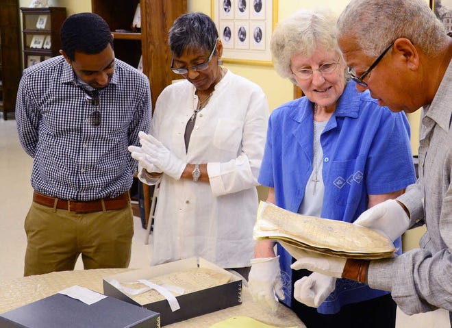 Sister Catherine Bitzer, archivist of the Diocese of St. Augustine, shows Bernard and Shirley Kinsey and their son Khalil Kinsey a document that records the marriage of two black St. Augustine residents in 1606 during a visit to the archives on Monday, July 23, 2012. The Kinseys are owners of a national recognized collection of African American art, which they are going to display in St. Augustine during the city's 450th celebration in 2015. By PETER WILLOTT, peter.willott@staugustine.com