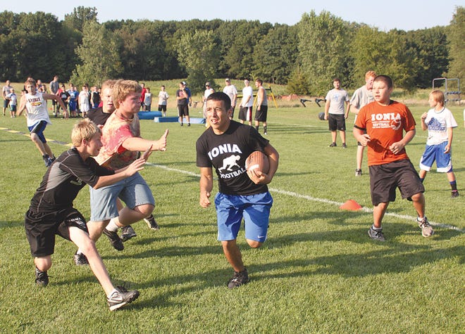 Ionia varsity football player Brandon Serna carries the ball while junior players, from left, Cameron Mahlich, Alex Bentley and Eric Butler close in Wednesday night during the Ionia Youth Football Camp.