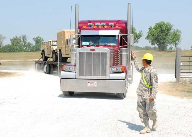Cpl. Somphone Sihavong, a transportation management coordinator with the 609th Movement Control Team from Fort Bragg, guides a commercial truck carrying tactical vehicles into the railhead and line-haul site July 25. Sihavong, a native of China Grove, N.C., is responsible for filing shipping paperwork attached to tactical vehicles and containerized units.